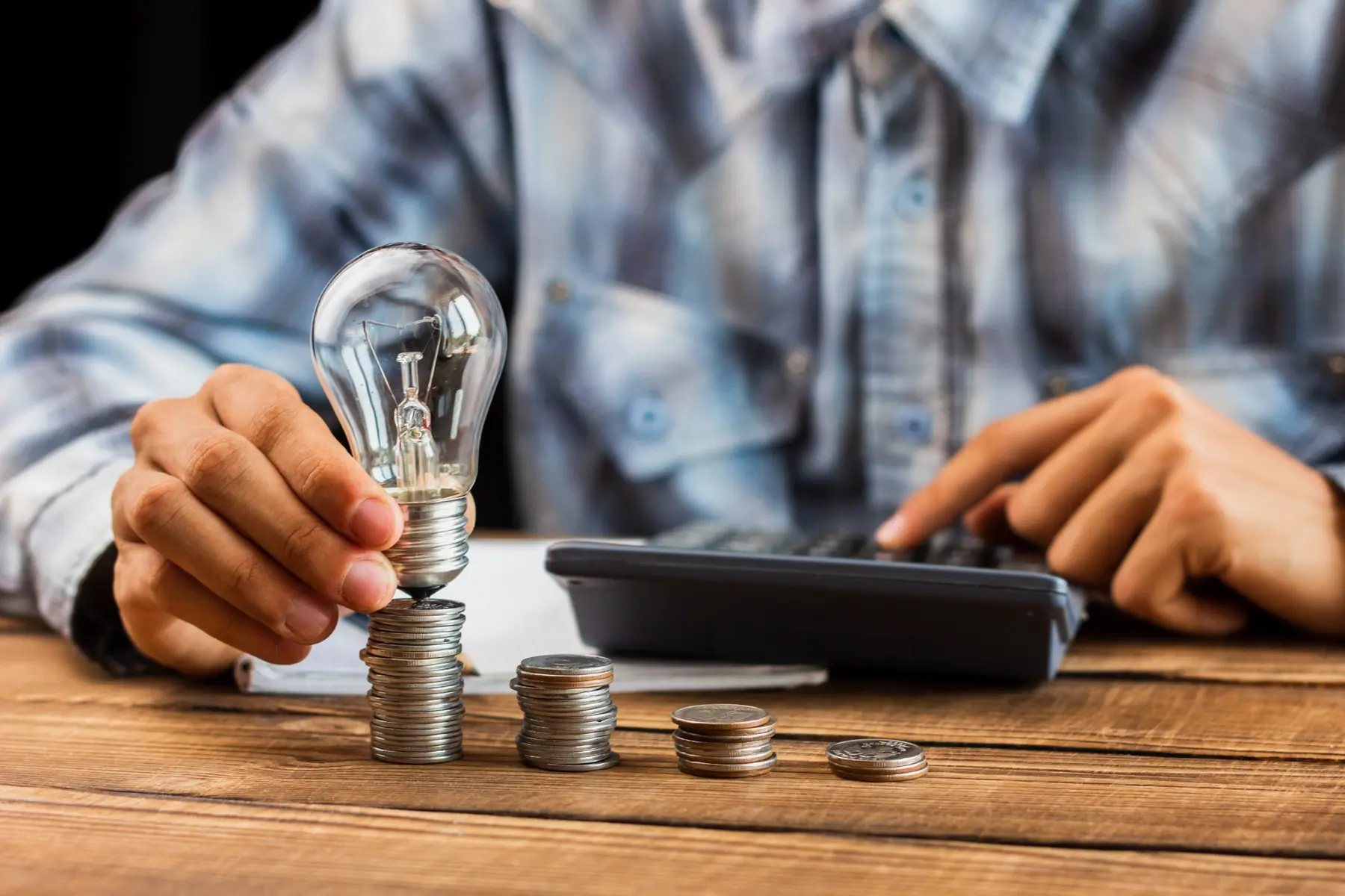 Businessperson calculating solar project value with coins and an energy-saving light bulb